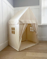 Beige children's play tent with window cutouts in a room with white walls and a window.