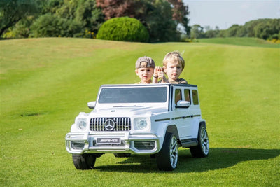 24V white Mercedes Benz G63 AMG 4x4 ride-on car for kids, featuring a realistic luxury SUV design, two seats, LED lights, working doors, and all-terrain wheels.