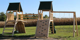 Cedar Peak Log Playground featuring double towers connected by a log bridge, with attached swings, slide, and tire swing for kids' outdoor play.